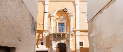 A narrow alleyway leading to a building with a balcony and a large arched door.