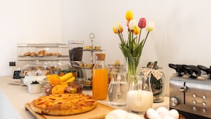 A breakfast buffet with a variety of food items, including a pizza, fruits, and a vase with tulips. - Palazzo de Luca (Fasano)