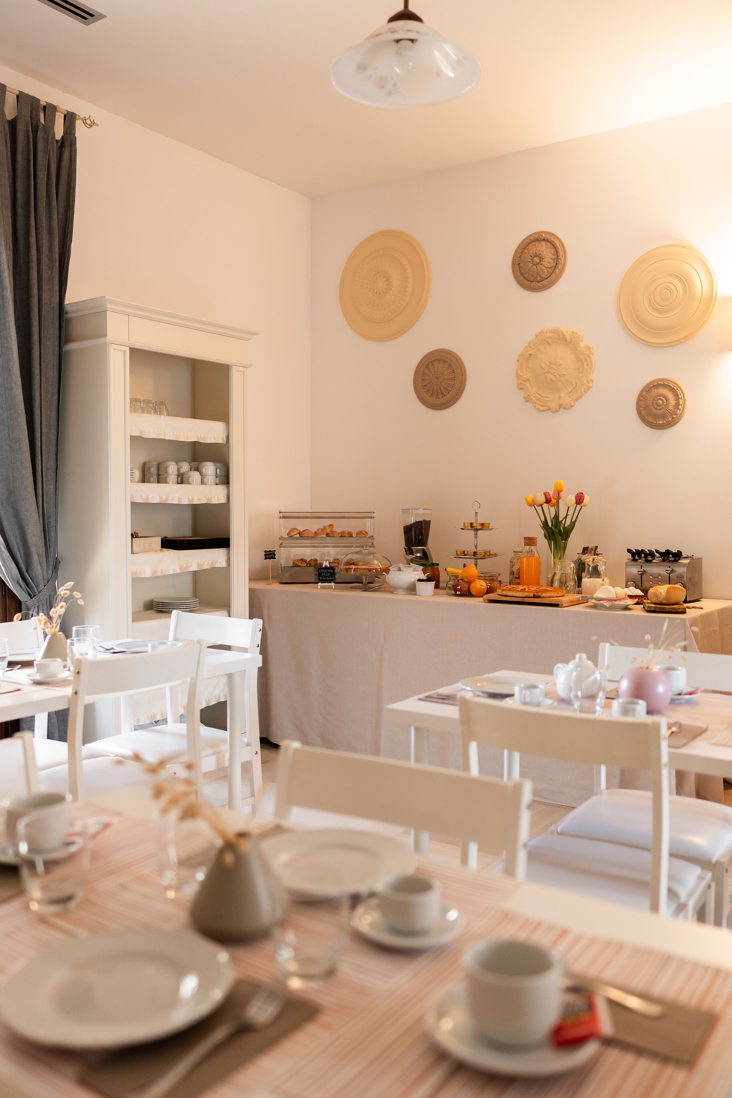 A dining area with white furniture, a buffet with various food items, and decorative plates on the wall.