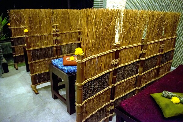 A room with a traditional woven partition, a wooden bed with a blue and white patterned bedspread, and a green cushion with a yellow flower. - Hotel Shri Ganesh (Buleleng)