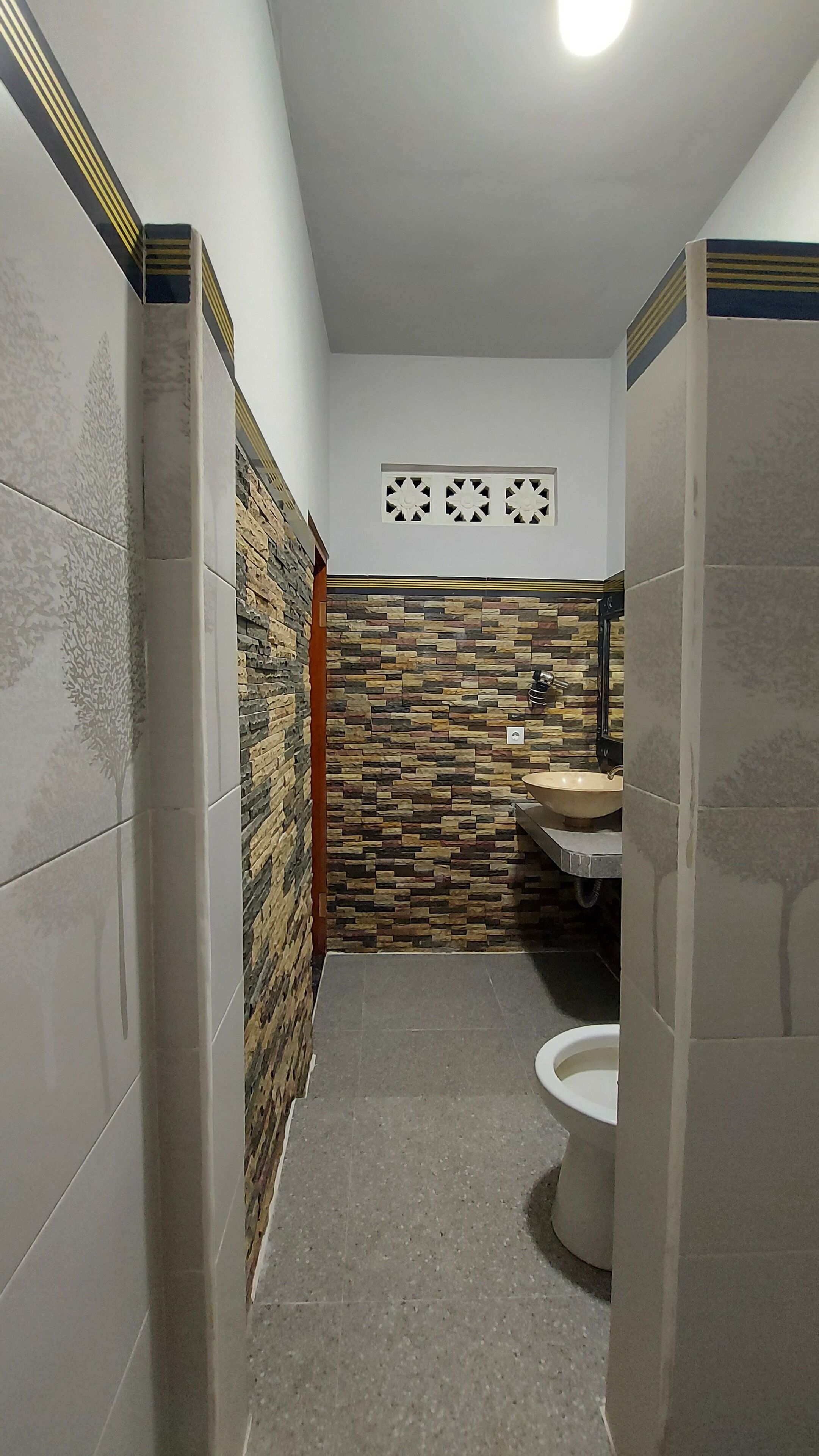 Een kleine badkamer met betegelde wanden, een accentmuur van steen, een wastafel en een toilet.