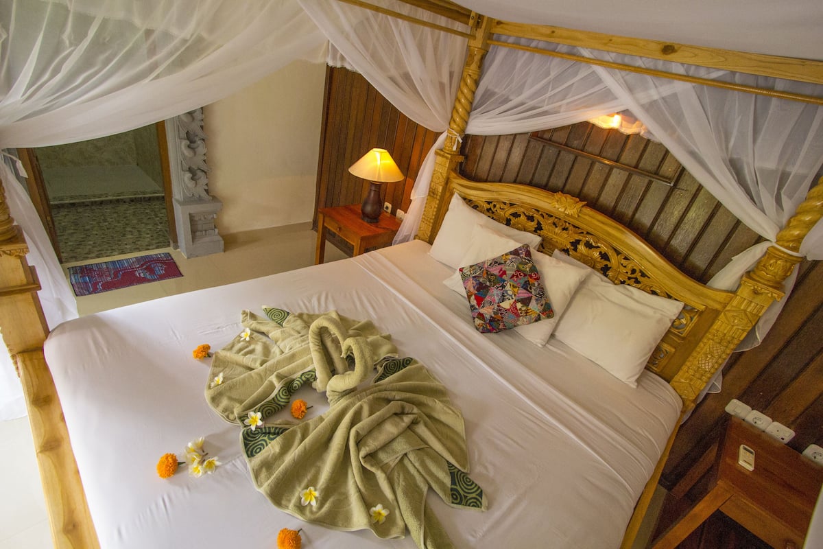 Una cama con dosel, una mesita de noche con lámpara y vista a una habitación con suelo estampado.