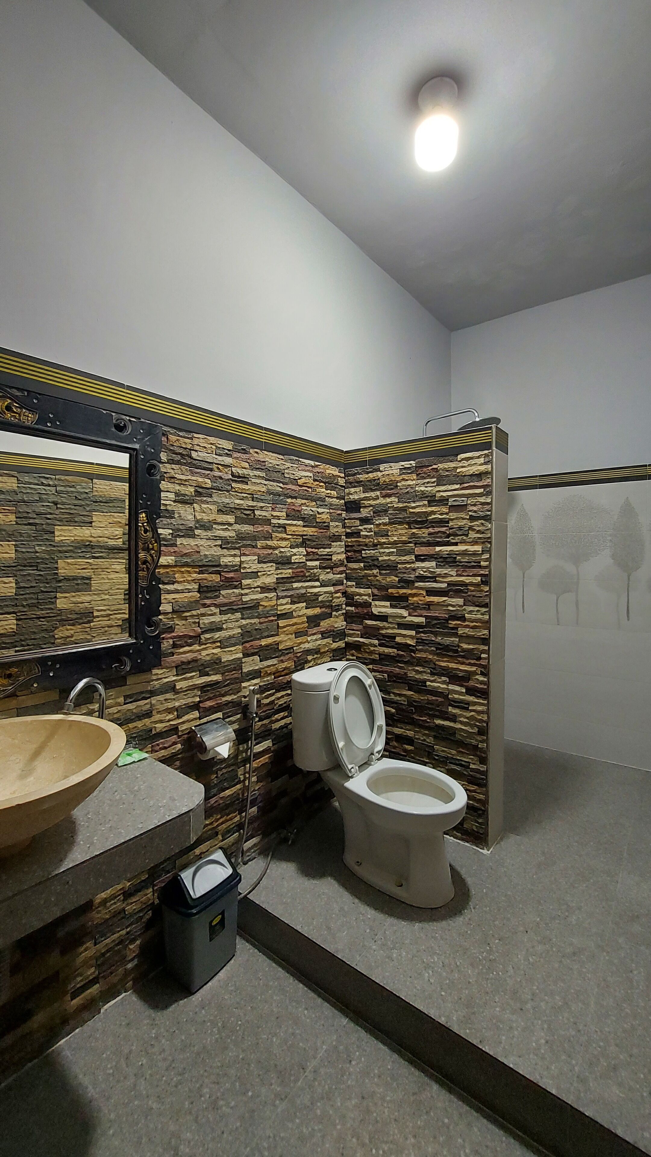 A bathroom with a stone wall, a wooden vanity, a sink, and two toilets.