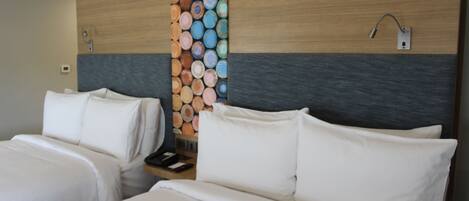 A hotel room with two beds, a wooden headboard, a wall with colorful wooden logs, and a nightstand with a lamp.