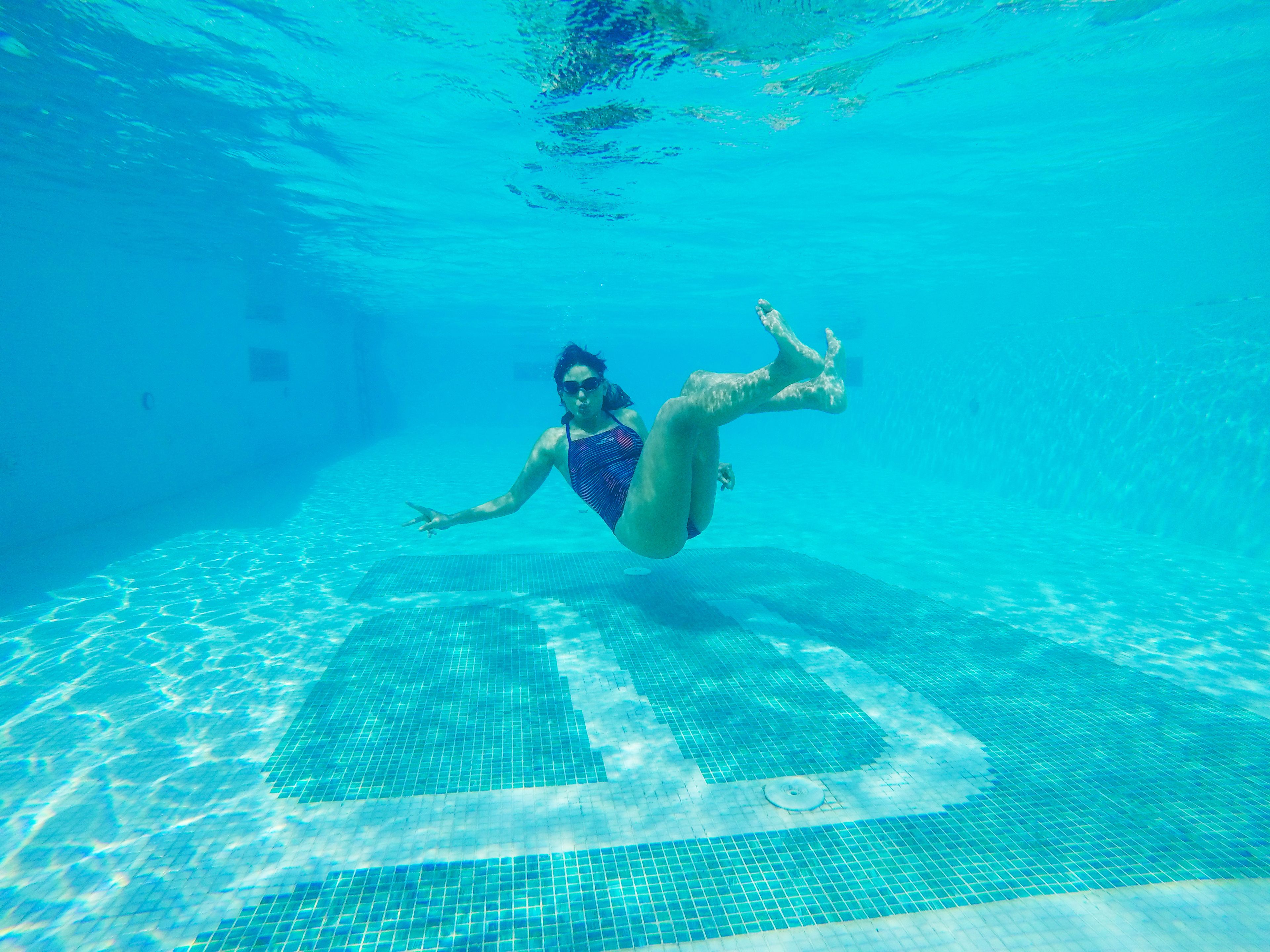 An underwater view of a swimming pool with a tiled floor and a person swimming.