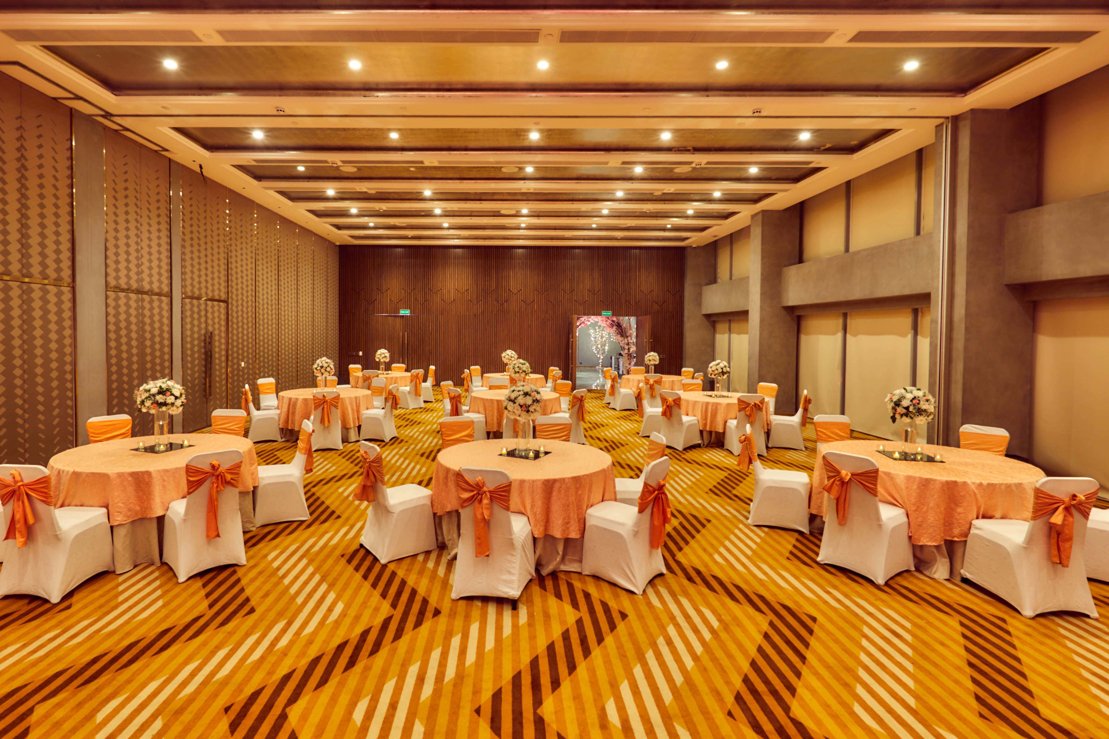 Une salle de banquet avec des tables rondes, des chaises blanches et des rubans orange.