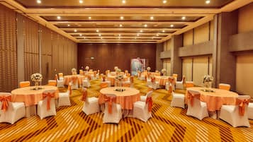 A banquet hall with round tables, white chairs, and orange sashes.