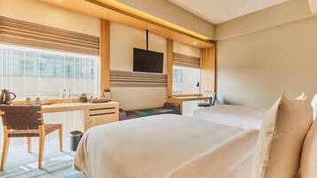Ein Hotelzimmer mit einem großen Bett, einem Schreibtisch mit Stuhl, einem an der Wand montierten Fernseher und einem Fenster mit Jalousien.