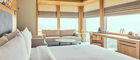 A modern hotel room with a large bed, a sofa, a small round table, and a kitchenette area.