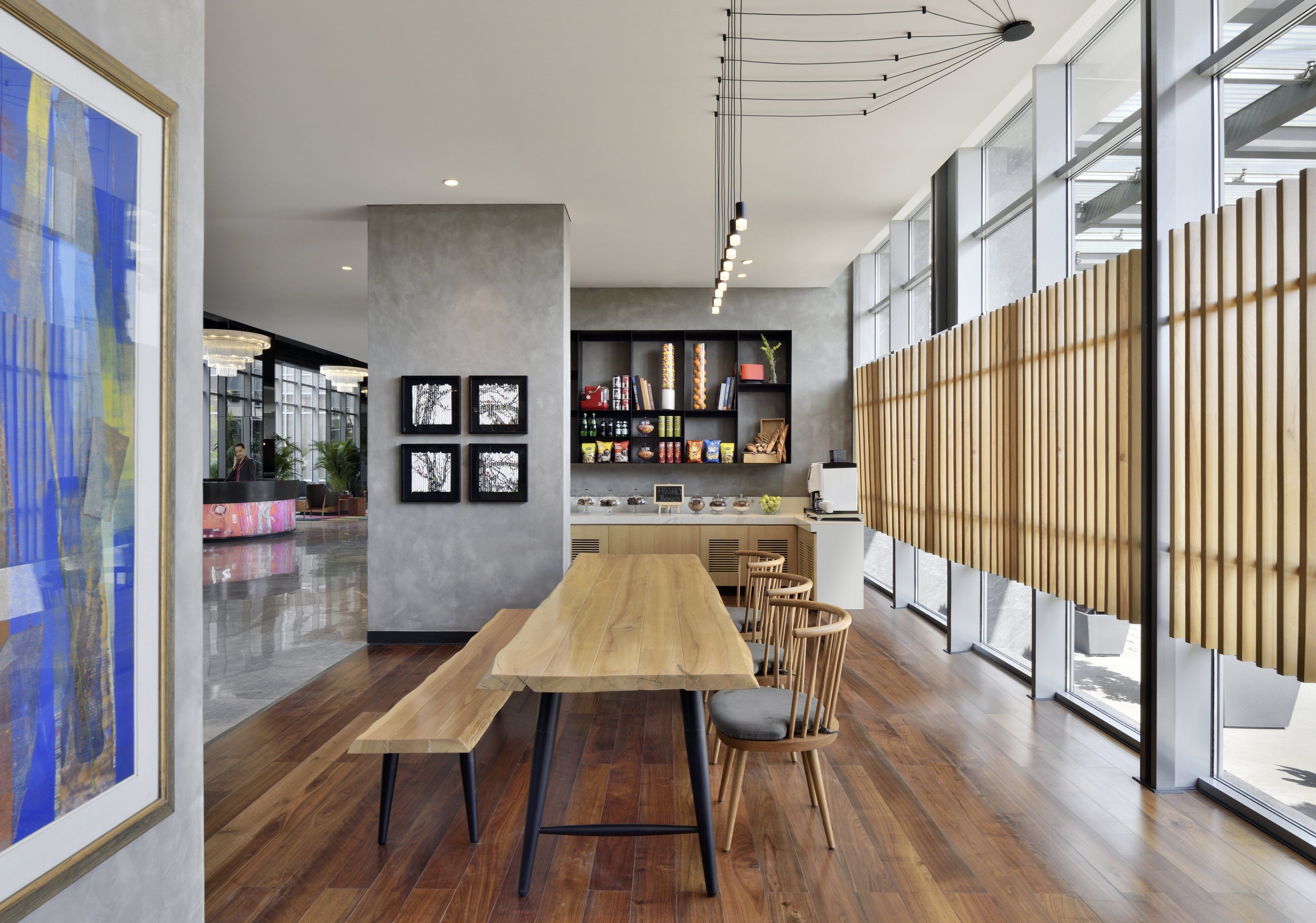A modern interior with a long wooden table and chairs, a kitchen area with shelves, and large windows.