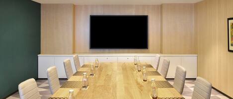 A conference room with a long table, chairs, a large screen, and a whiteboard.