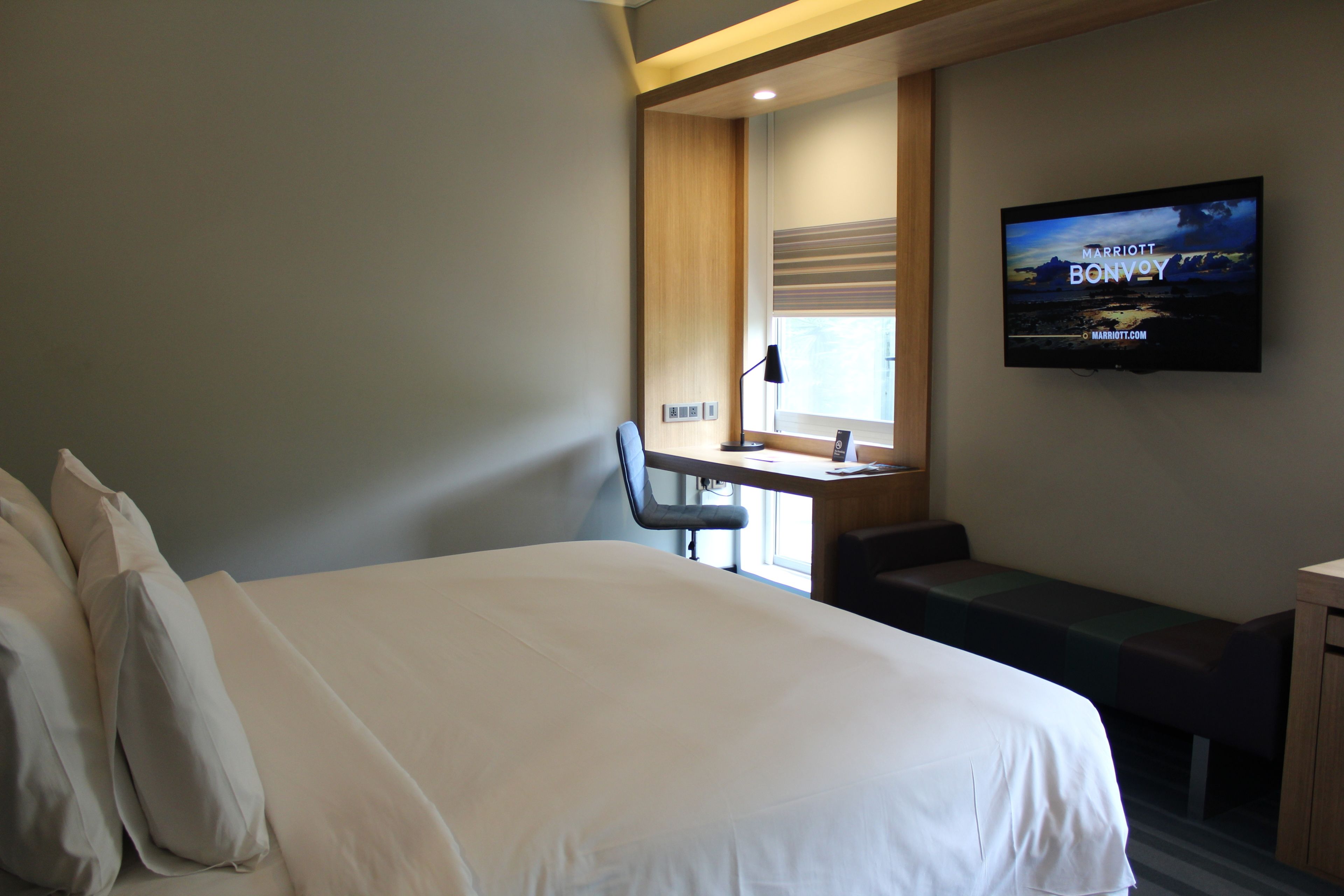 A hotel room with a large bed, a desk, a chair, and a television displaying 'Marriott Bonvoy'.