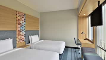 A hotel room with two beds, a desk, a bench, and a large window.