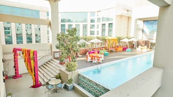 A rooftop pool area with a clear view of the cityscape, outdoor seating, and a staircase leading to an upper level.