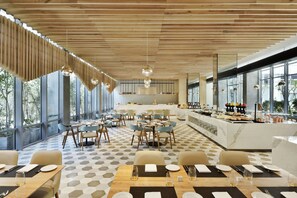 A modern restaurant with a geometric floor pattern, wooden ceiling slats, and large windows offering a view of the outdoors. - Aloft by Marriott New Delhi Aerocity (New Delhi)
