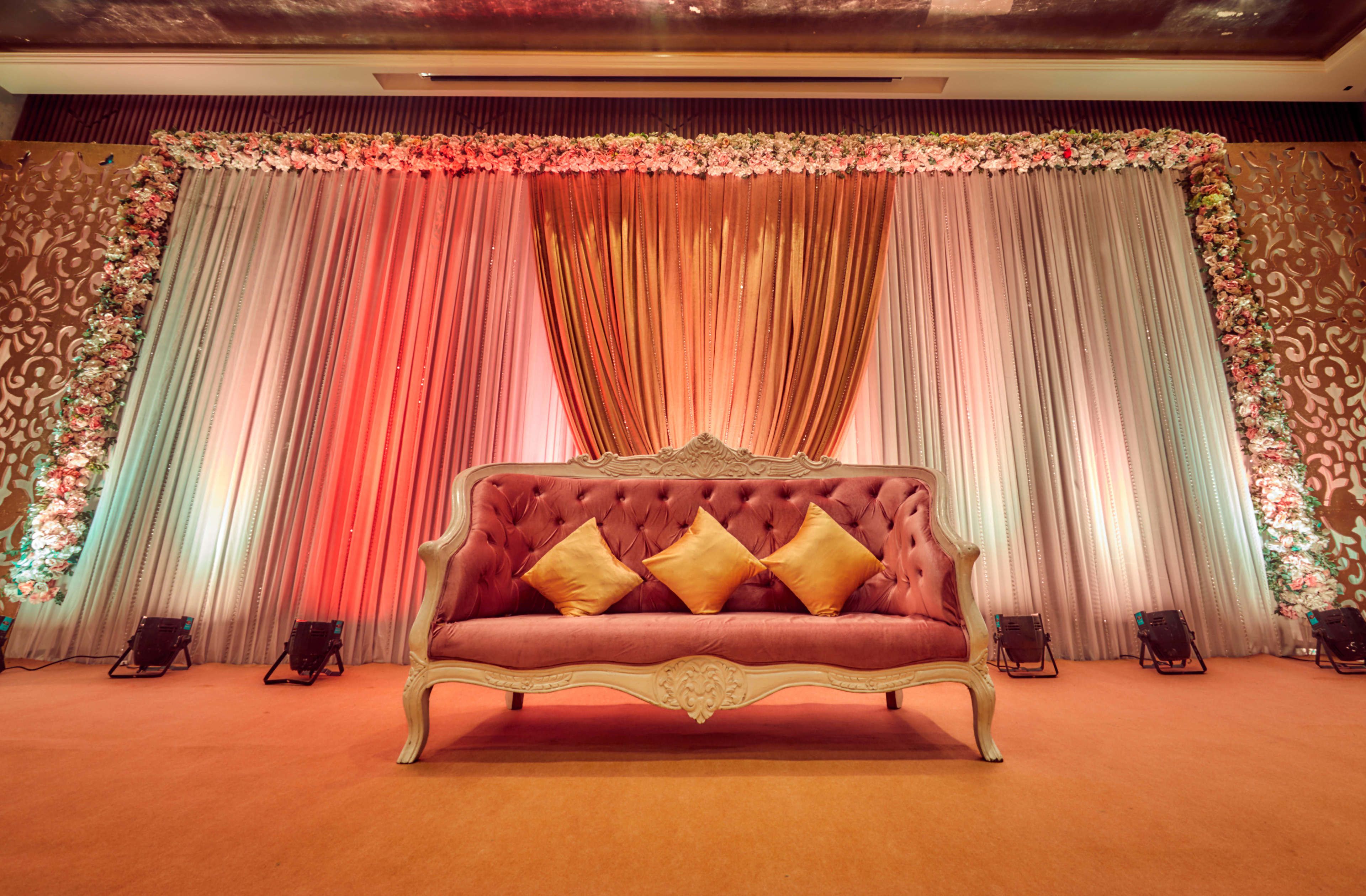 A stage with a red sofa and gold cushions, flanked by draped curtains and floral decorations.