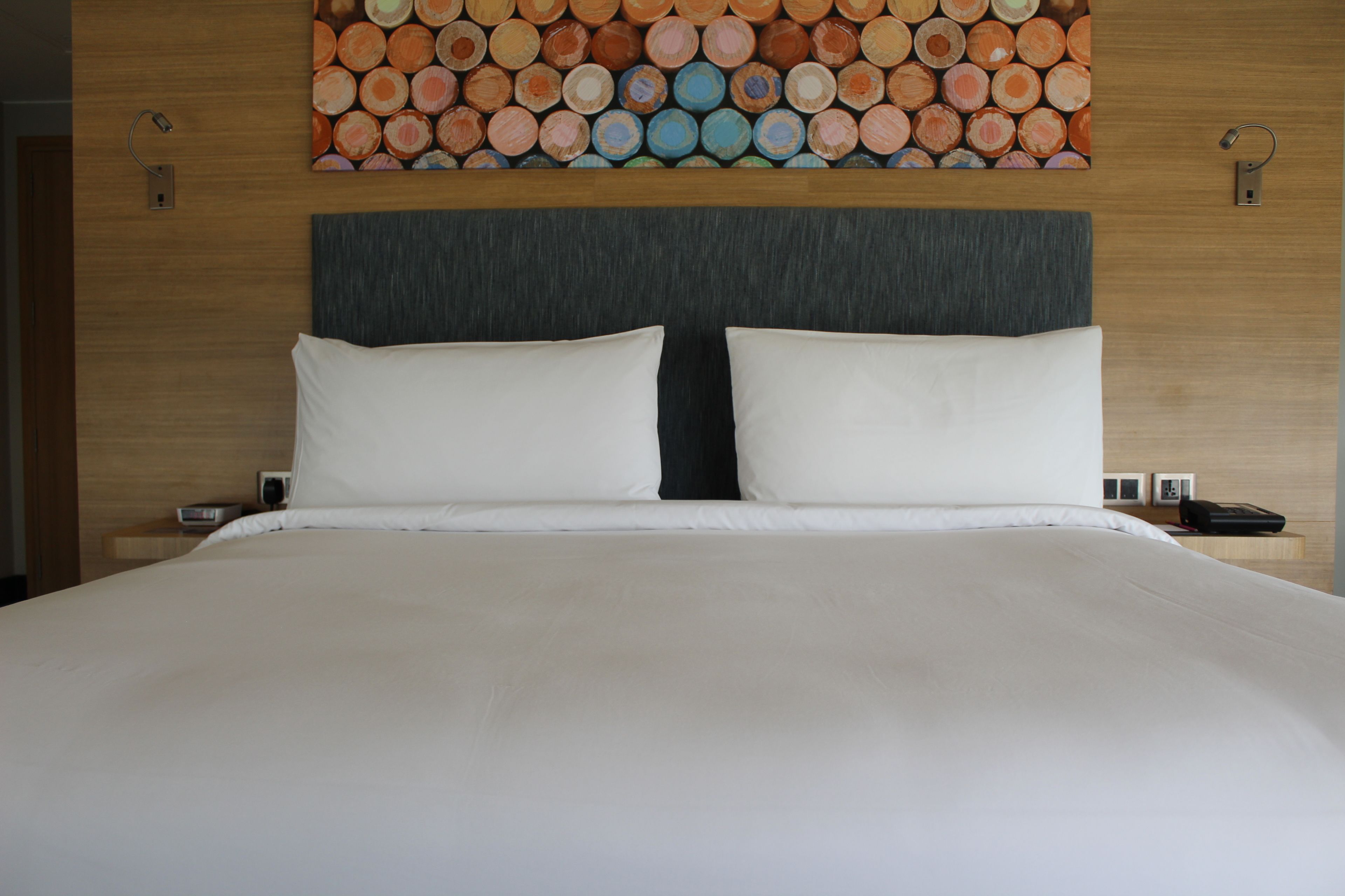 A neatly made bed with white bedding, a dark headboard, and a wall art of painted logs above.