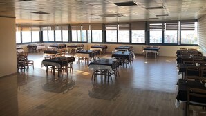 A spacious dining area with multiple tables and chairs, large windows with blinds, and a high ceiling with ventilation ducts. - Kilim Otel (Sanliurfa)