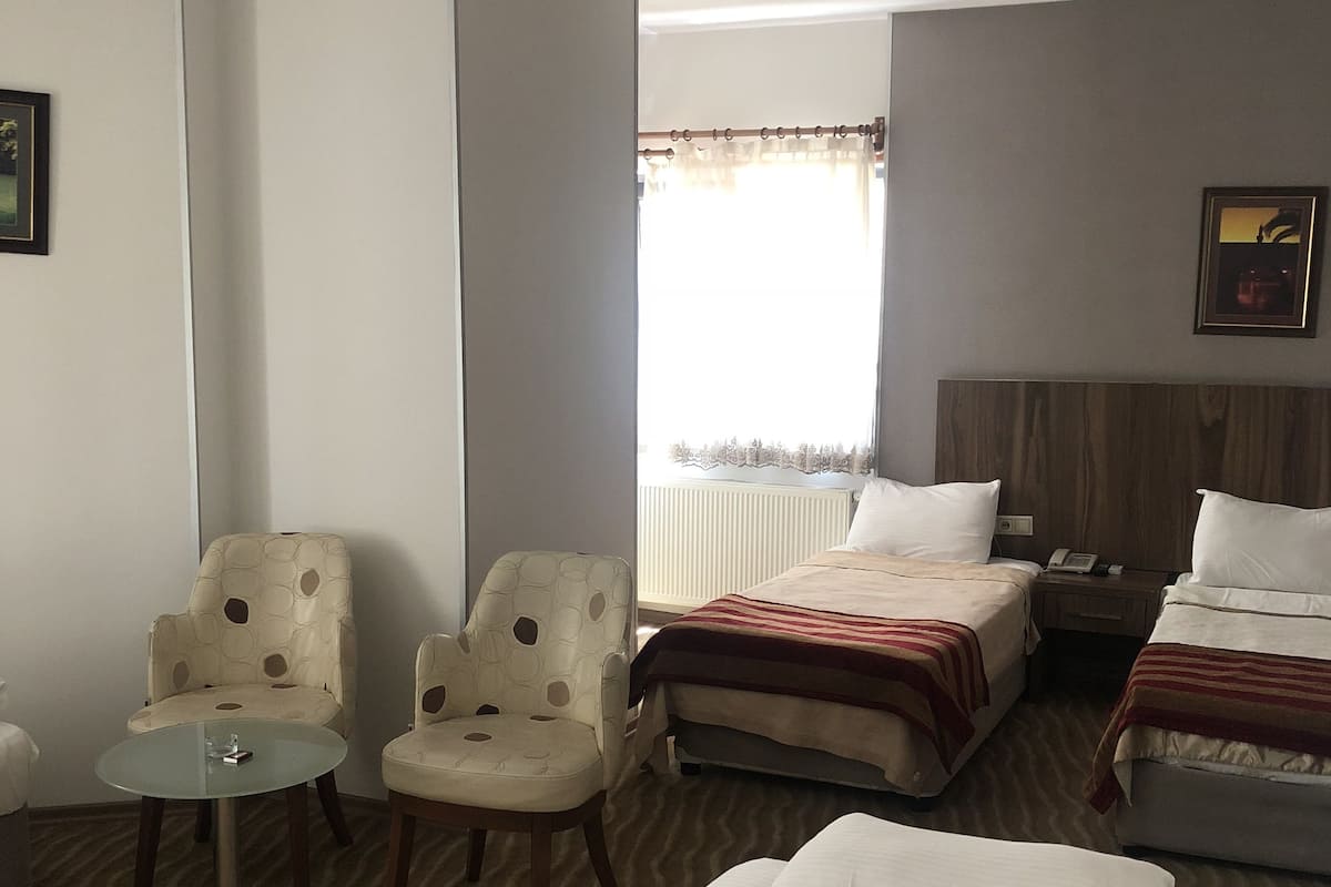 A hotel room with two single beds, a double bed, a small table, two armchairs, and a window with curtains.