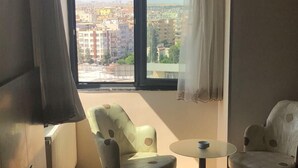 A hotel room with a bed, a desk with a keyboard, two chairs, a small table, and a window with a view of buildings. - Kilim Otel (Sanliurfa)