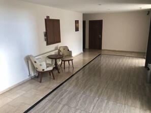 A hallway with a tiled floor, two chairs, a small round table, and a door at the end. - Kilim Otel (Sanliurfa)