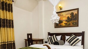 A hotel room with a wooden bed, striped bedspread, a painting of a sunset, a white canopy, and a chair.