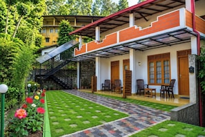 A covered outdoor area with a staircase leading to a building, a small garden with flowers, and outdoor seating. - Dinaro Guest (Ella)