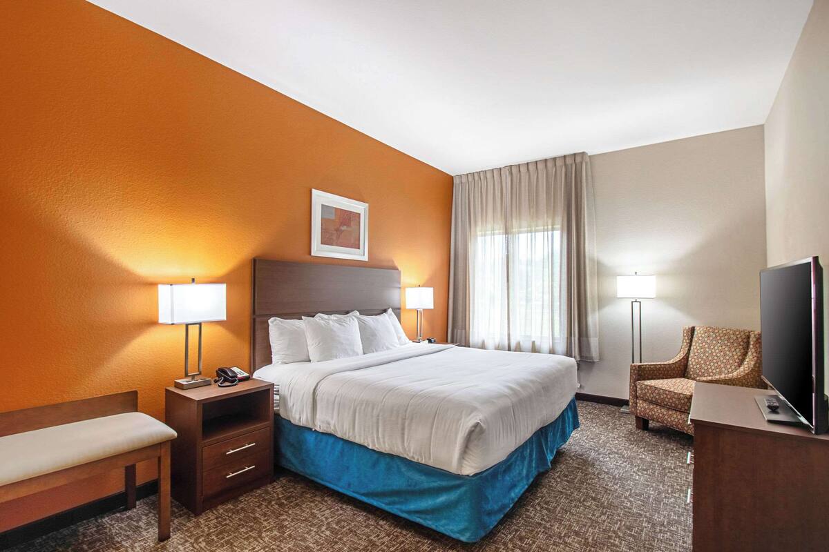 A hotel room with a large bed, bedside lamps, a desk with a television, and a chair.