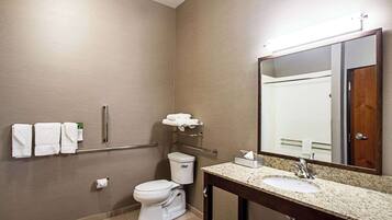 A bathroom with a toilet, sink, and mirror. There are towels on a rack and a toilet paper holder.