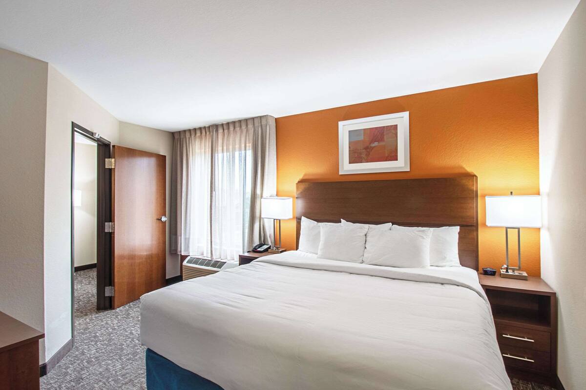 A hotel room with a large bed, two bedside tables with lamps, a wooden headboard, and a framed picture on the wall.
