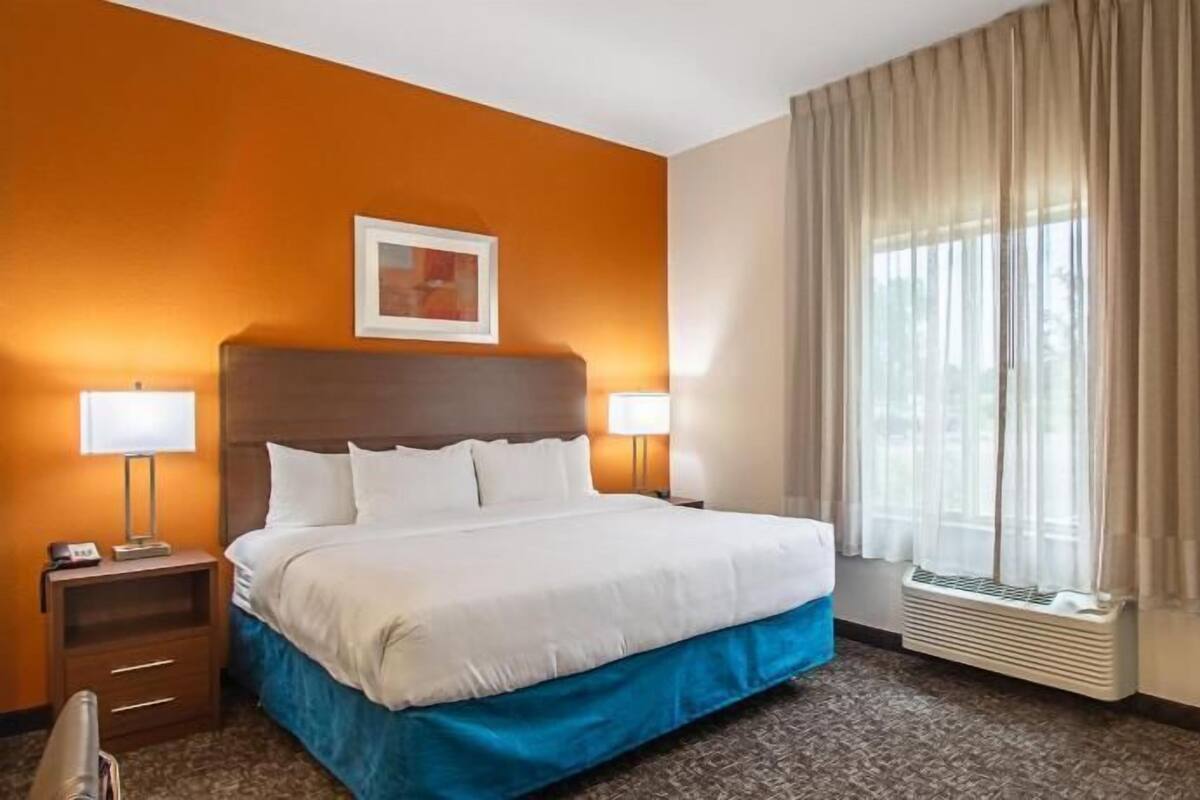 A hotel room with a bed, two bedside lamps, a nightstand, a window with curtains, and a television.
