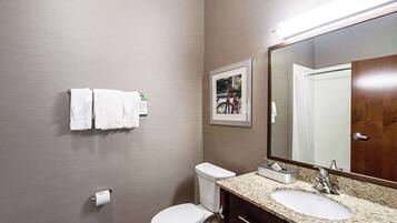 A bathroom with a toilet, sink, and mirror. There are towels hanging on the wall and a picture frame.