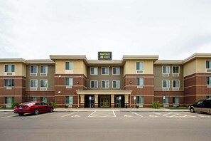 A MainStay Suites hotel with a brick facade, multiple windows, and a parking lot with cars.