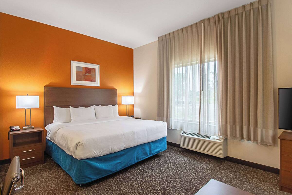 A hotel room with a large bed, two bedside tables with lamps, a window with curtains, and a wall-mounted TV.
