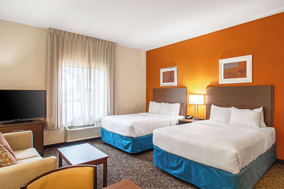 A hotel room with two beds, a TV, a desk, and a chair.