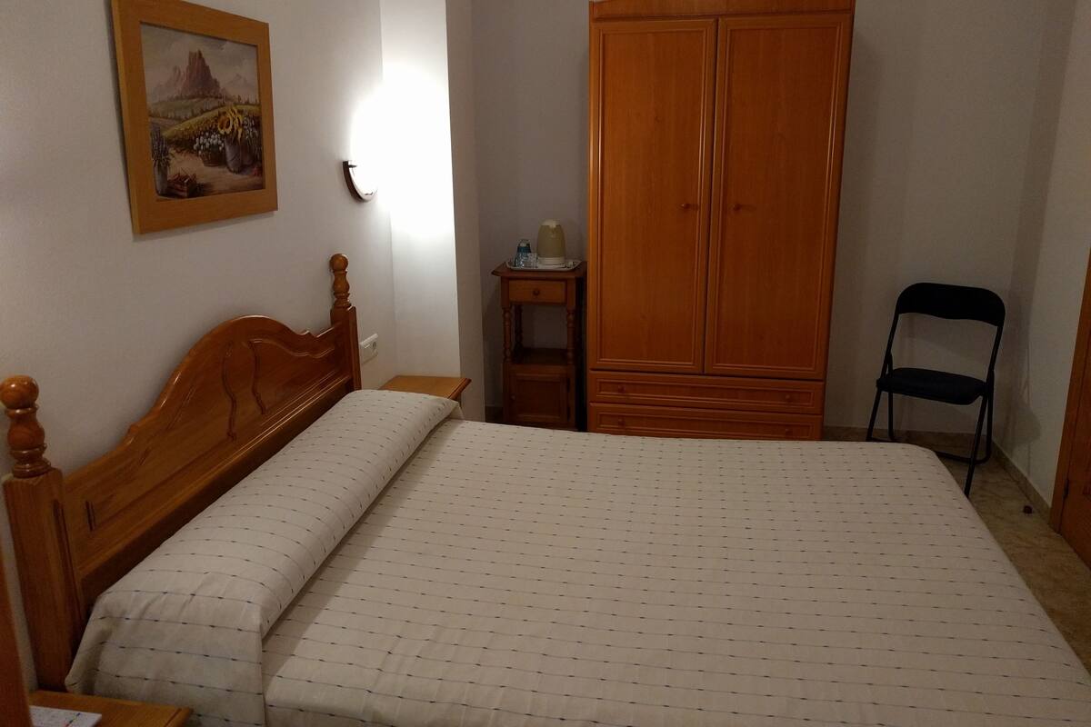 Un dormitorio con una cama de madera, un armario, una silla y un cuadro en la pared.