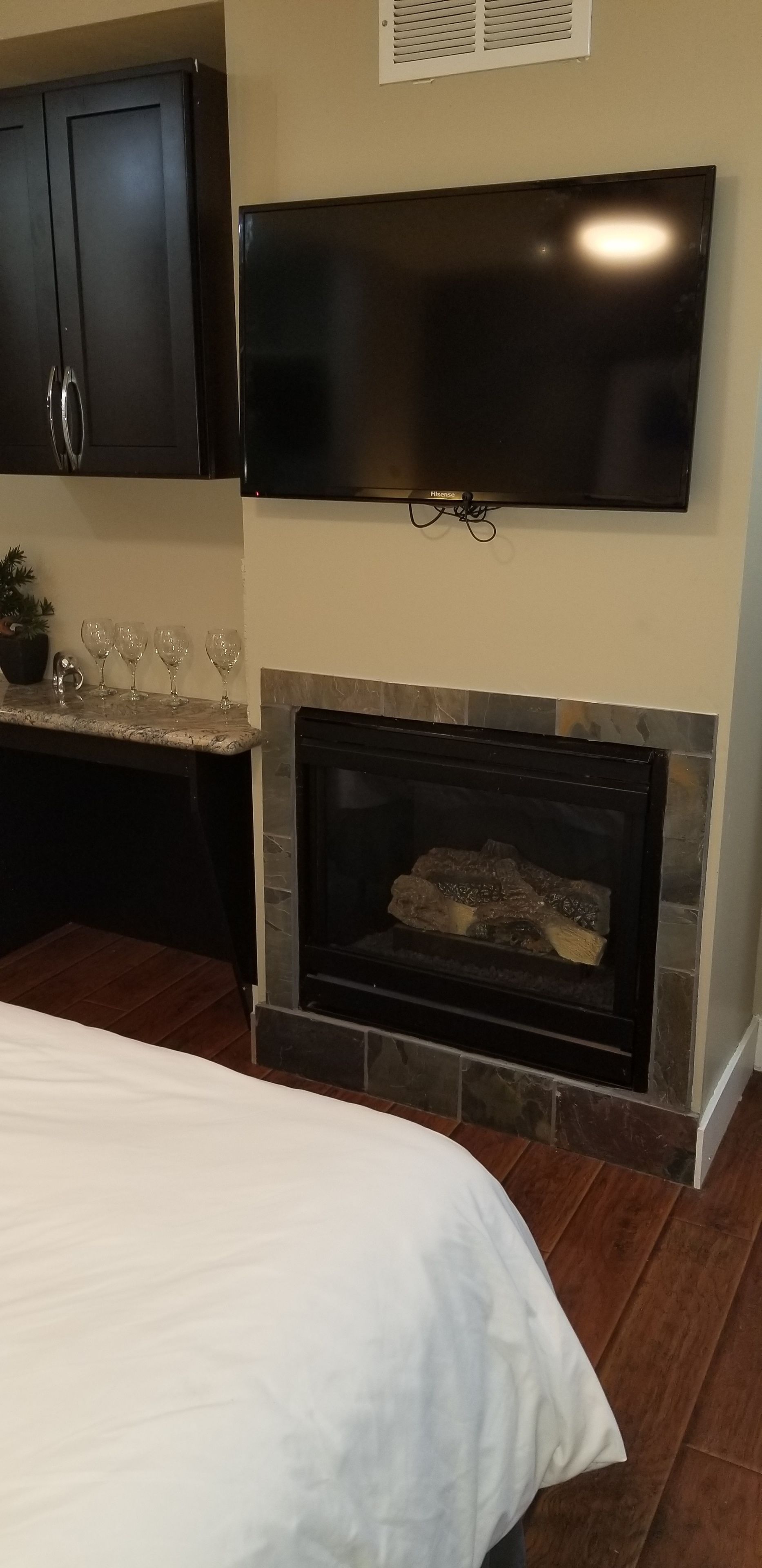 A bedroom with a bed, a fireplace, a TV mounted above it, and dark wooden cabinets.