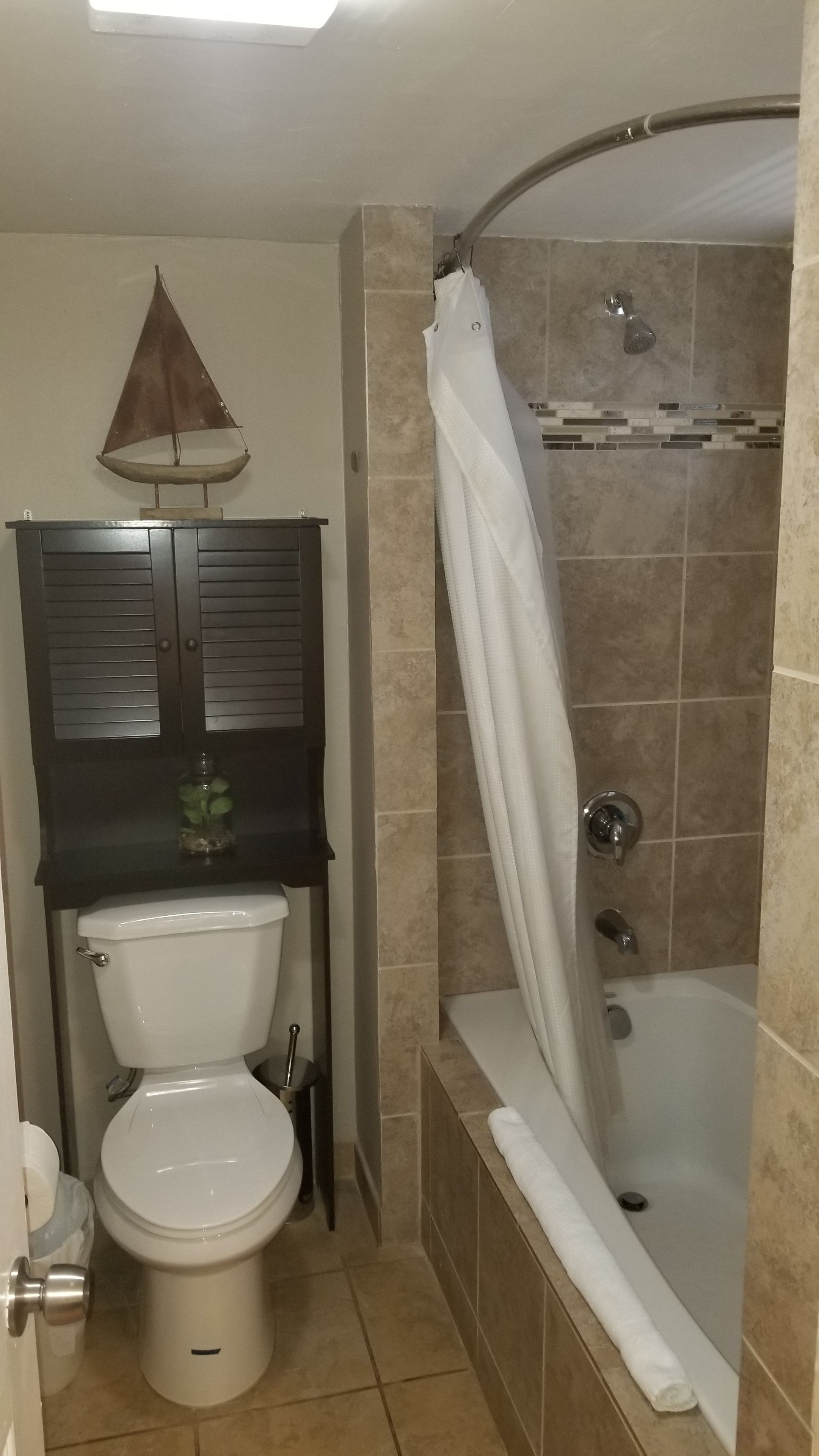 A bathroom with a toilet, a sink, a shower with a curved tub, and a towel rack.