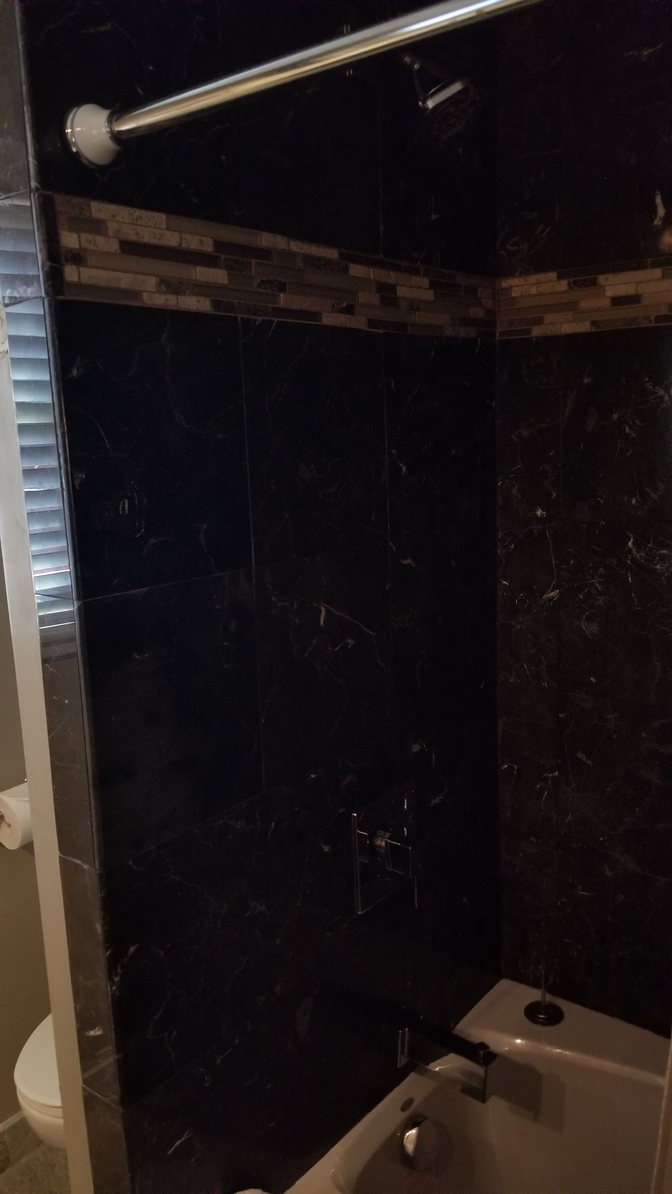Un baño con pared de mármol oscuro, cabina de ducha de vidrio, bañera blanca y un inodoro.