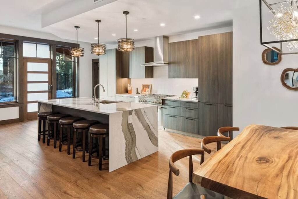 A modern kitchen with a large island, bar stools, and a dining table.