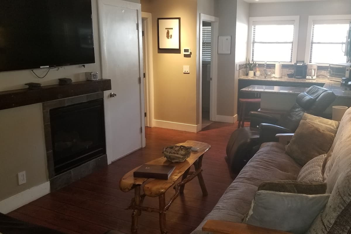 Ein Wohnzimmer mit Kamin, Wand-Fernseher, Couchtisch aus Holz und einer Couch.