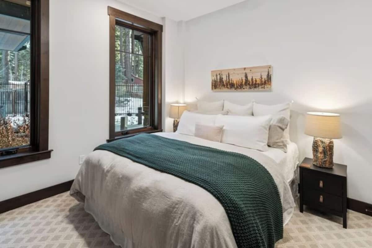 Ein Schlafzimmer mit einem großen Bett, einem Fenster, einem Nachttisch und einer Wandlampe.