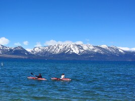 Dos kayakistas en un lago tranquilo con montañas nevadas al fondo.