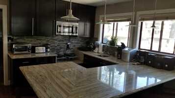 A modern kitchen with dark cabinets, a large island, a built-in oven, and a window with a view of the outside.