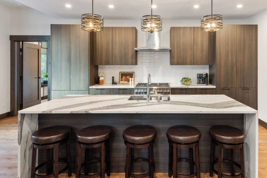 A modern kitchen with a large island, bar stools, and pendant lighting.