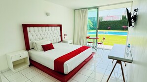A hotel room with a large bed, a small table, and a view of a swimming pool. - Hotel Palmas Cocoyoc (Yautepec)