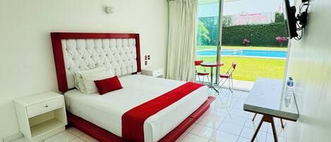 Een hotelkamer met een groot bed, een kleine tafel en uitzicht op een zwembad.