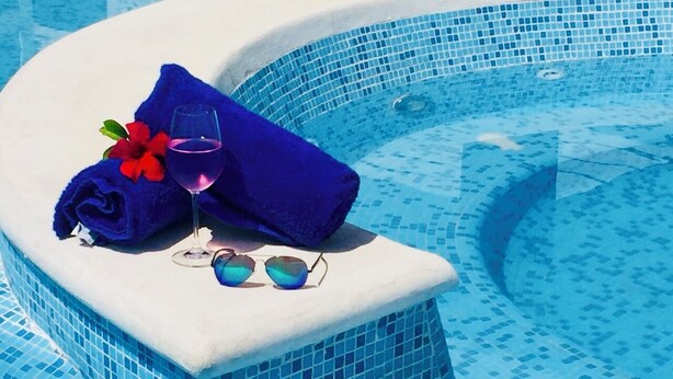 A hot tub with a blue mosaic tile interior, a rolled blue towel, a glass of wine, and a pair of sunglasses on the edge. - Hotel Palmas Cocoyoc (Yautepec)
