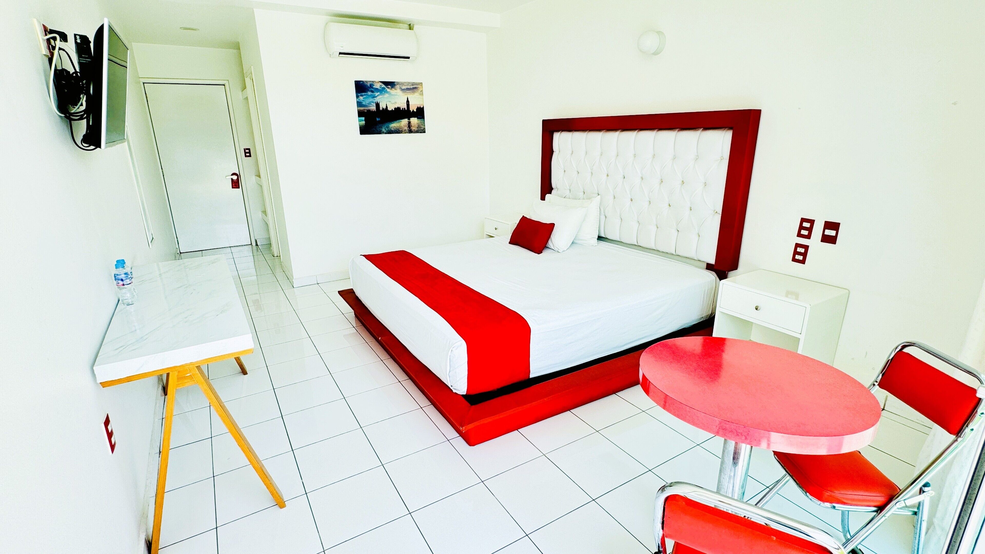A hotel room with a bed, a desk, a chair, and a small table.