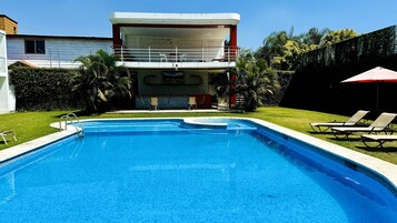Una piscina al aire libre, sombrillas, sillones reclinables de piscina